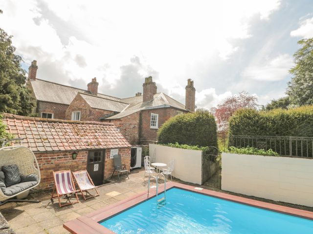 An outdoor area with a small pool two deck chairs a hanging chair a round table with two chairs and a brick house at Wolds Way Great Driffield