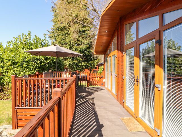 An outdoor wooden deck with patio furniture and an umbrella next to a building with large glass doors at Bowness 66 in Troutbeck Bridge