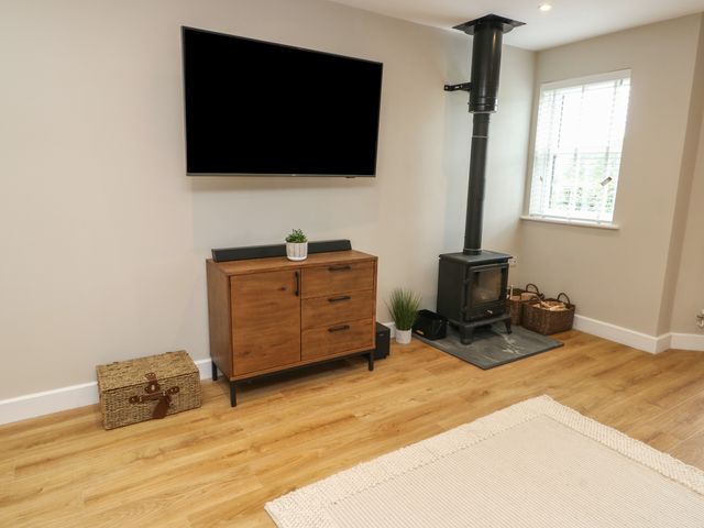 A living room with a mounted television a wooden cabinet and a wood burning stove at Bay Tree Cottage in Llanrug