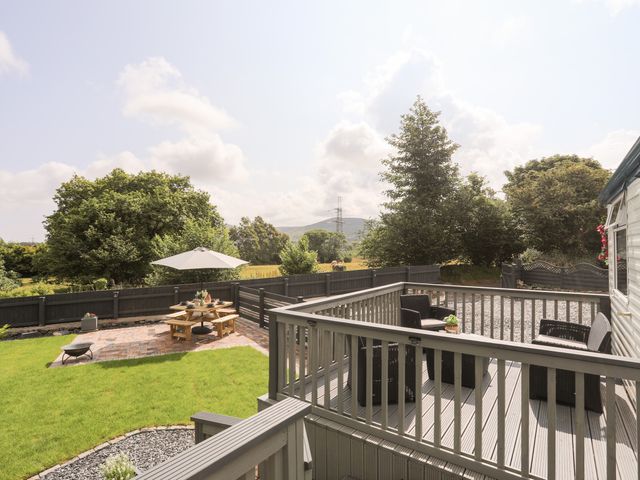 An outdoor patio with chairs and a table and a garden area with a wooden picnic table and umbrella at Tyn Clwt in Penisa'r Waun near Llanrug