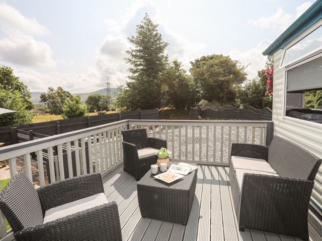 A patio with black wicker furniture including two chairs a loveseat and a table with plants cups and snacks at Tyn Clwt in Penisa'r Waun near Llanrug