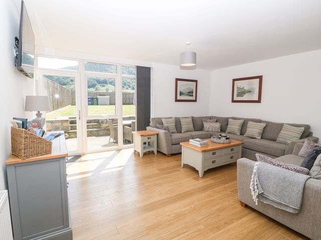 A living room with a large gray sectional sofa and wooden coffee tables near glass doors opening to a garden at 3 Pensyflog Barns in Porthmadog