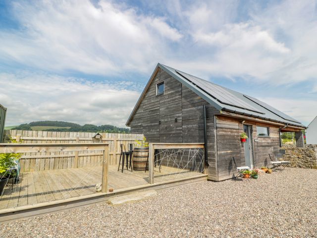 A wooden house with solar panels on the roof a deck area with chairs and a barrel at Fasgadh in Inchyra near Errol