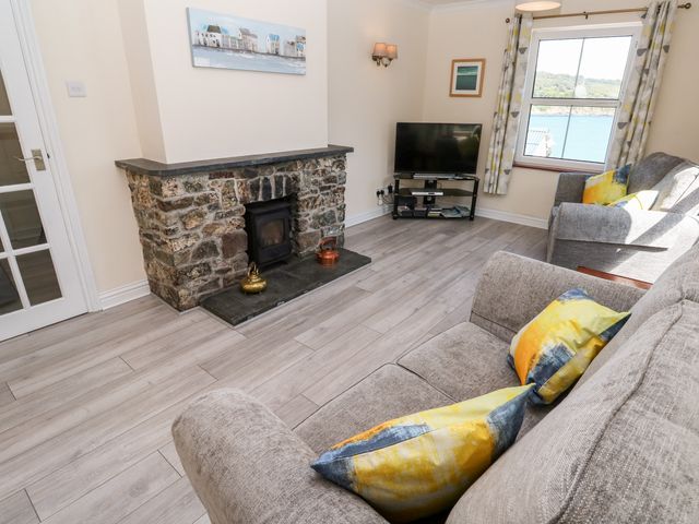 A living room with a stone fireplace two couches with yellow and blue cushions a television and a window overlooking water at The Mariners in Coverack