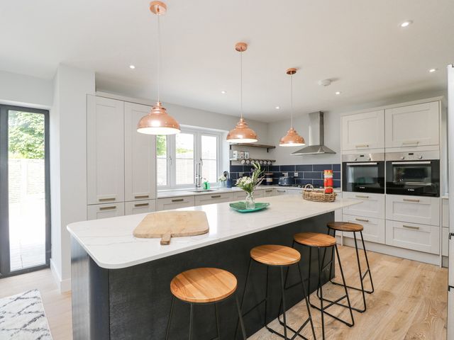A kitchen with a large island and four stools under copper pendant lights at Greystones in Upton St Leonards