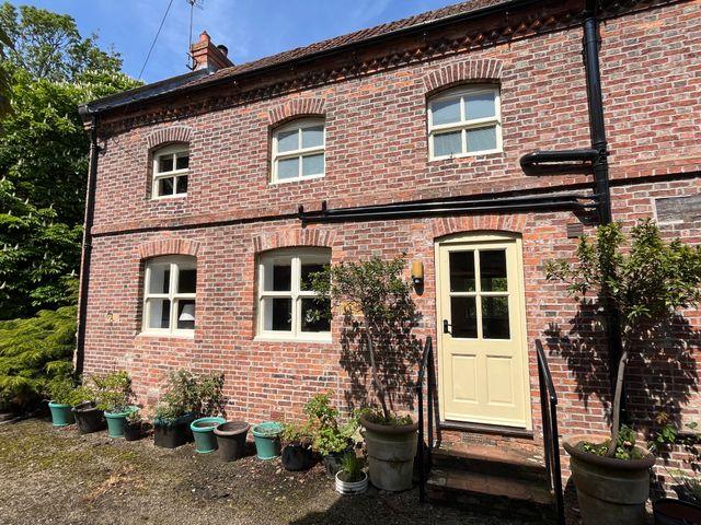A brick exterior wall with multiple windows a cream door and several potted plants outside at The Old Barn in Caenby