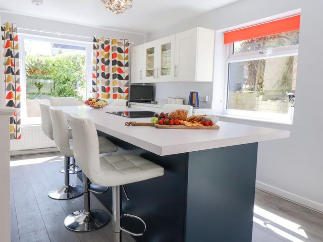 A kitchen with a large white countertop island with bar stools and colorful curtains at Tan Parc in Morfa Nefyn