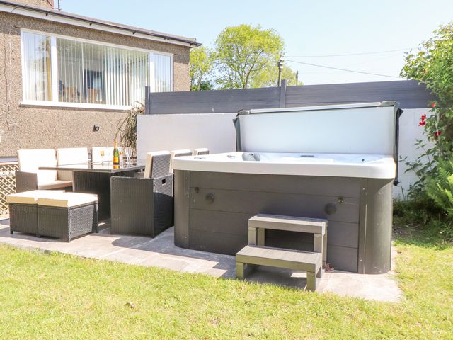 An outdoor patio area with a hot tub and a dining table with chairs at Tan Parc in Morfa Nefyn