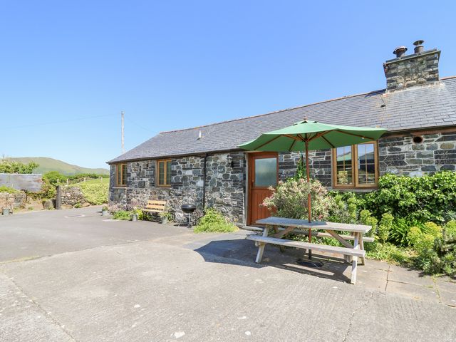 A stone cottage with a wooden bench and barbecue outside and a picnic table with green umbrella at Swn y Nant in Tywyn