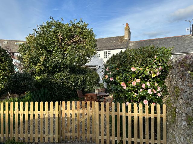 A garden with a wooden fence, a table with chairs, bushes with flowers and a house in the background at 1 Dolphin Cottages in Lyme Regis