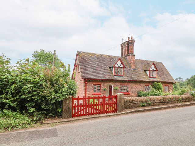 A brick cottage with red window frames and a red gate beside a stone wall at 1 Fountain Cottages in Peckforton Tarporley