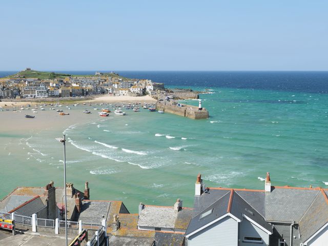 A coastal town with houses boats and a pier extending into the sea at Waves End in St Ives