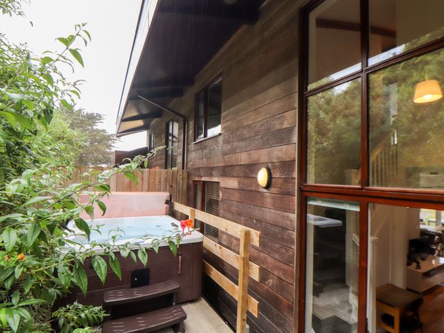An outdoor hot tub next to a wooden building with windows and a light at Garras in Porthtowan