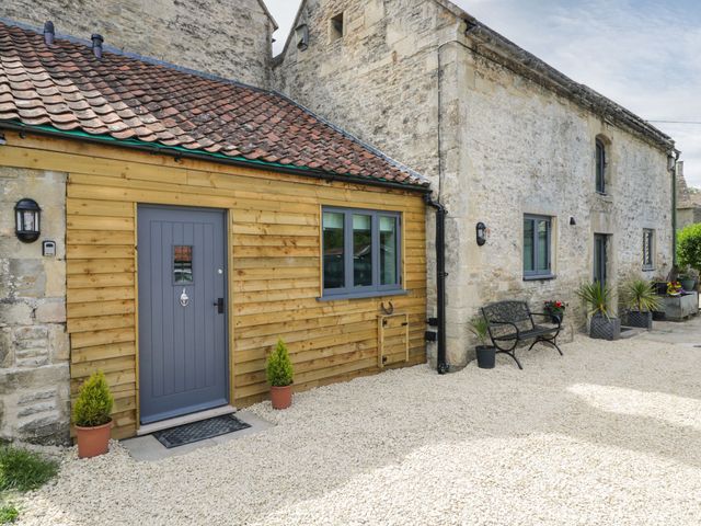 Exterior of a stone building with a gray door, windows, potted plants, and a bench at Chequers Barn in Corsham