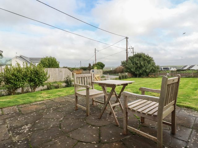 A patio with two wooden chairs and a small wooden table on a paved surface overlooking a grassy yard at Freefolk Cottage in Polzeath