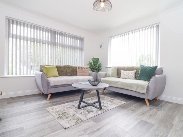 A living room with two sofas, a round coffee table, a small rug, and vertical blinds on windows at Apple Tree Bungalow in Lanner