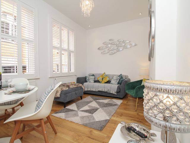 A living room with a gray sofa, green chair, patterned rug, dining table, white chairs, and wall art at The Cottage in Weymouth