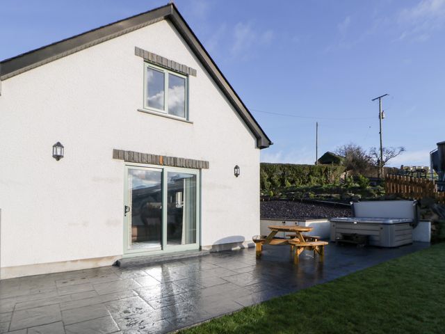 An outdoor view of a house with a patio, table, and hot tub at Beudy near Llanilar