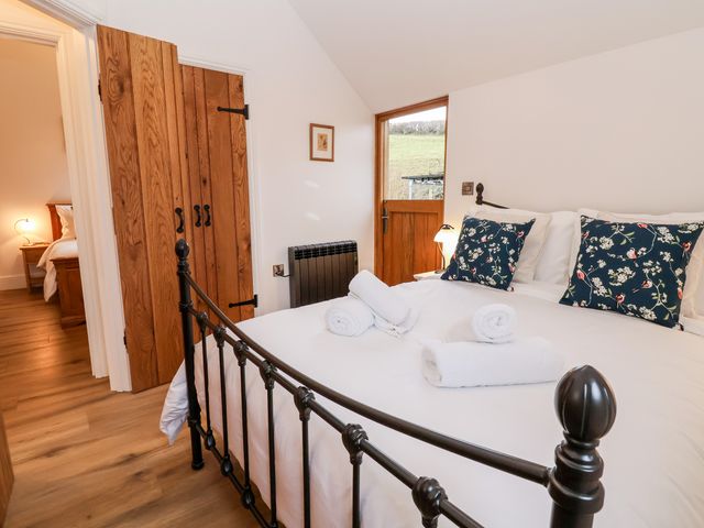 A bedroom with a metal bed frame white bedding floral pillows wooden door and a window showing outside at Rockhill Farm Hay Barn in Clun