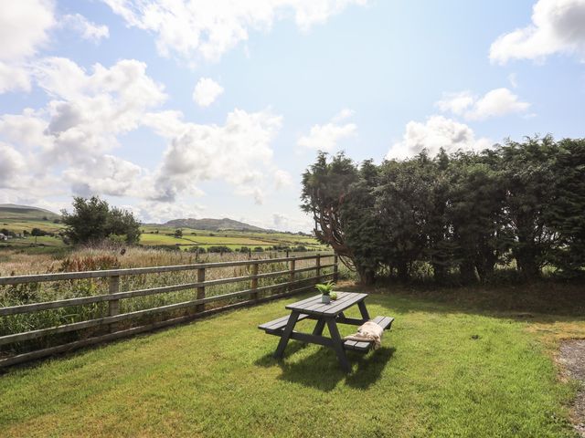 A garden with a wooden picnic table and bench near a wooden fence and trees at Bwthyn Derwin Fawr in Garndolbenmaen near Penygroes