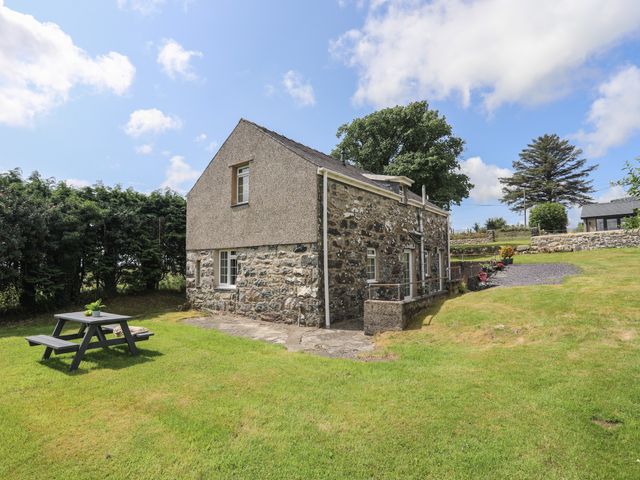 A stone and pebble dash house with a grassy yard and picnic table at Bwthyn Derwin Fawr in Garndolbenmaen near Penygroes