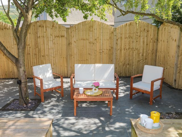 An outdoor seating area with wooden chairs and a table under a tree in a fenced yard at Maes Y Ffynnon in Nefyn