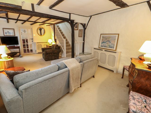 A living room with sofas armchair a wooden dresser table lamps wall art and staircase at Poppy Cottage in Beaminster
