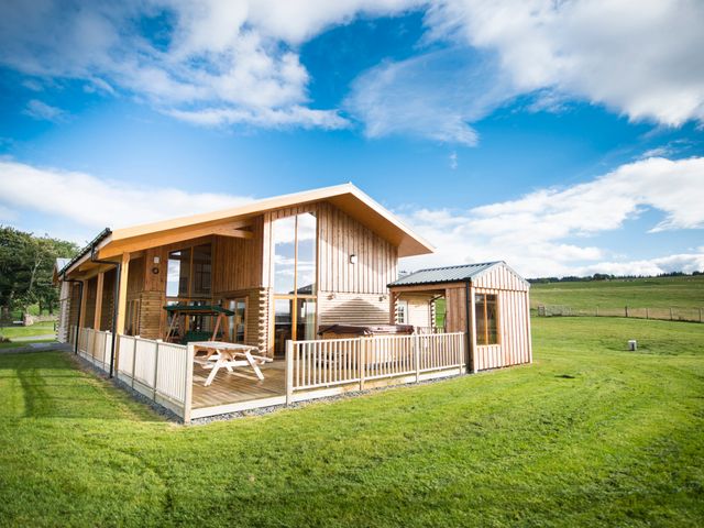 A wooden house with a fenced porch and picnic table on grass at Aurae in Cawdor near Inverness