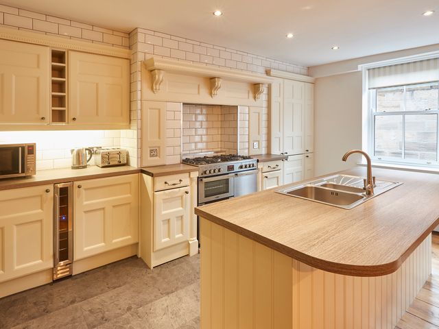 A kitchen with cream cabinetry a gas stove a microwave kettle toaster and an island with a sink at Sanders House in Whitby