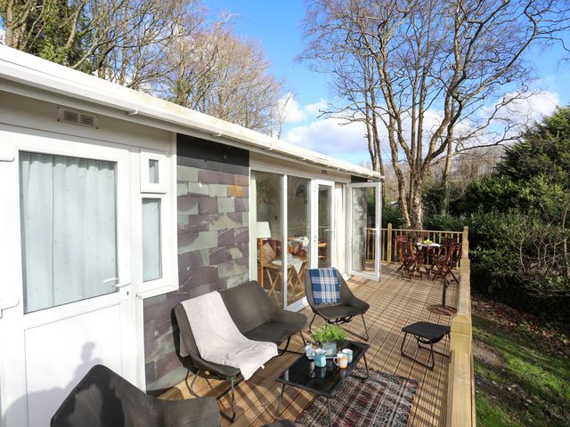 An outdoor wooden deck with chairs tables and a small plant at Treetops in Caernarfon
