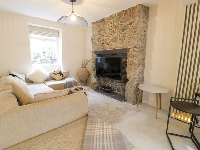A living room with a beige sectional sofa a stone fireplace with a mounted TV and small tables at Hendre in Menai Bridge