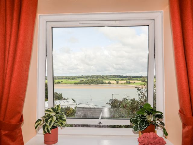 A window with two potted plants on the sill looking out to a river and green fields at 12 Brynffynnon in Y Felinheli