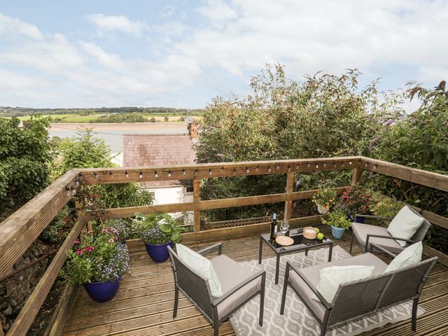 An outdoor wooden deck with seating area and table overlooking a river at 12 Brynffynnon in Y Felinheli
