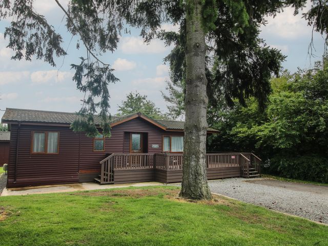 A wooden cabin with a deck surrounded by trees and grass at Foxglove in Eardisland