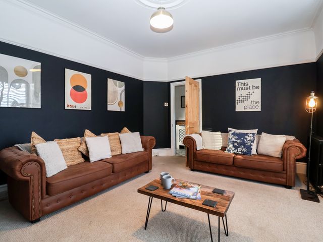 A living room with two brown sofas a wooden coffee table and three modern art prints on dark walls at Sunrise House in Pakefield near Lowestoft