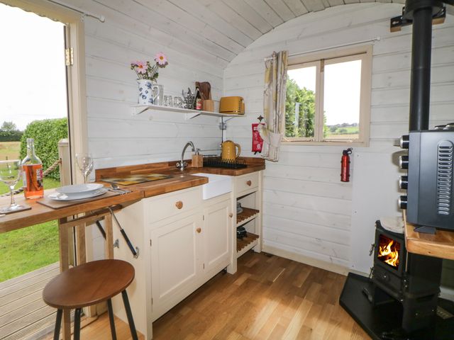 A small kitchen with wooden countertops a sink a window a stove with fire and an open door at Floras Hut in Liskeard