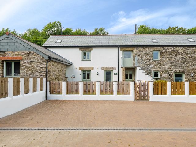 The exterior of a stone and white plaster house with a pitched roof and a small fenced yard at The Granary in Davidstow near Camelford