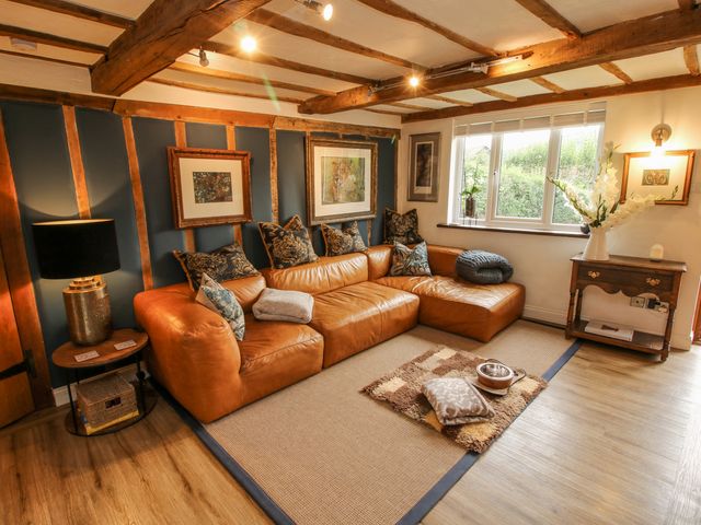 A living room with a tan leather sectional sofa and cushions a wooden side table with a lamp and framed pictures on the wall at Pen Y Groes in Berriew