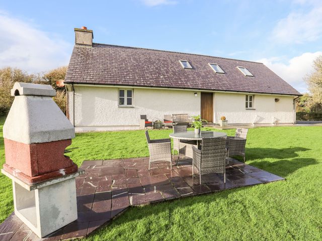 An outdoor patio with a table and chairs next to a barbecue grill in front of a house with skylights and a wooden door at Rhyd Y Bont Bach in Rhoscolyn