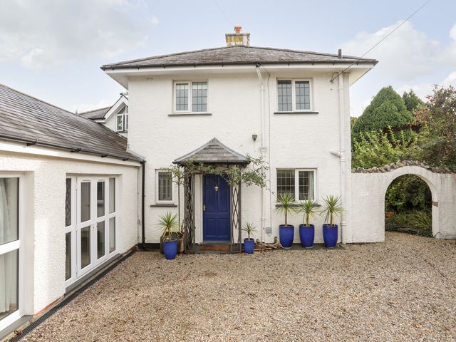 A white two-story house with a blue front door and blue pots with plants on a gravel driveway at Bwthyn in Borth-y-Gest near Porthmadog