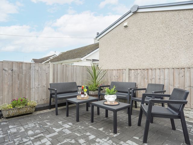 An outdoor patio with black chairs and tables with plants and a bottle of wine at Rhiwlas Bach in Benllech