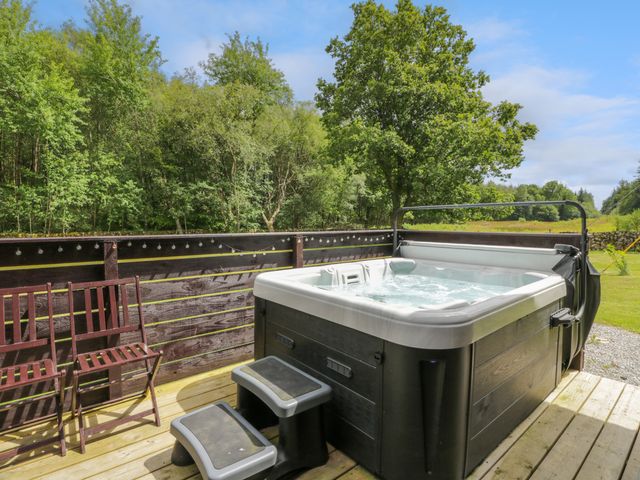 An outdoor hot tub with steps next to wooden chairs on a wooden deck surrounded by trees at Glenisle in Dalbeattie