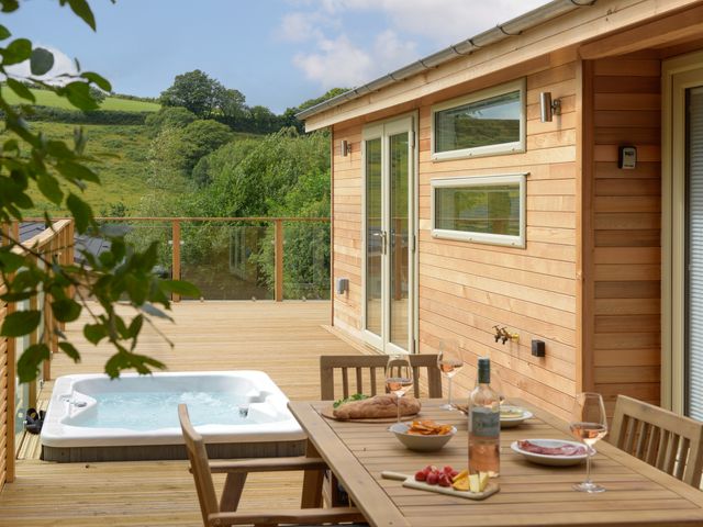 A wooden outdoor deck with a hot tub and a dining table set with food and drinks at 4 Valley View in Lanreath