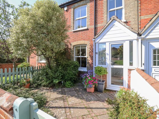 A front garden with plants flowers and a tree outside a brick house with a white porch at Green Gate Cottage Reydon near Southwold