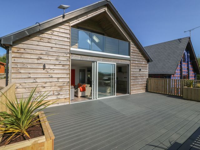 A wooden house with a deck and glass doors at The Hideaway in Mynytho near Abersoch