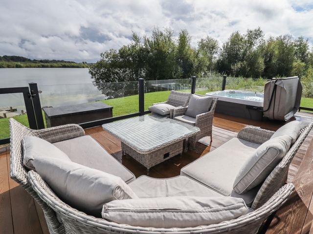 An outdoor deck with wicker seating and a glass table overlooking a lake with trees at 40 Delamere Point in Delamere