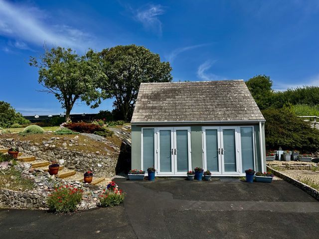 A shed with large windows and potted flowers at Tower Cottage Near Pembroke