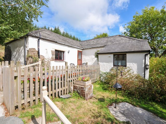 A cottage surrounded by a fence and flower bed at Windbury Cottage in Hartland