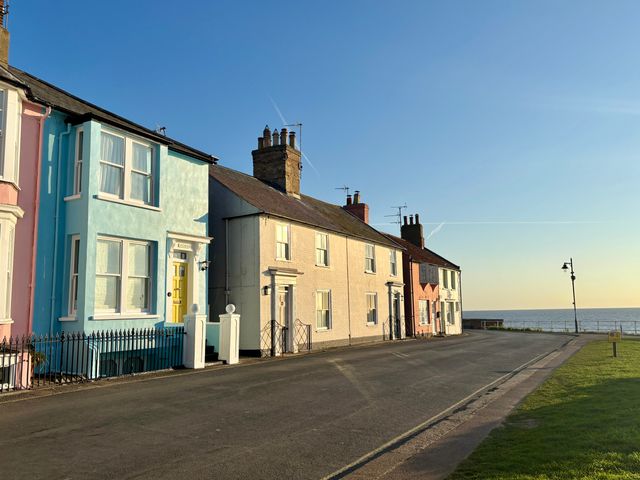 A row of houses along a street with the sea visible in the background at Astondene East Cliff in Southwold