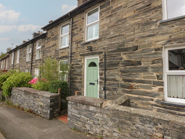 A stone house exterior with a green door and flower hedge at Chandos in Dolwyddelan